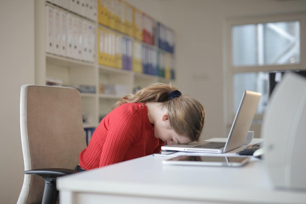 Vrouw in kantoor met burn-out, met haar hoofd op laptop, worstelend met stress en vermoeidheid.