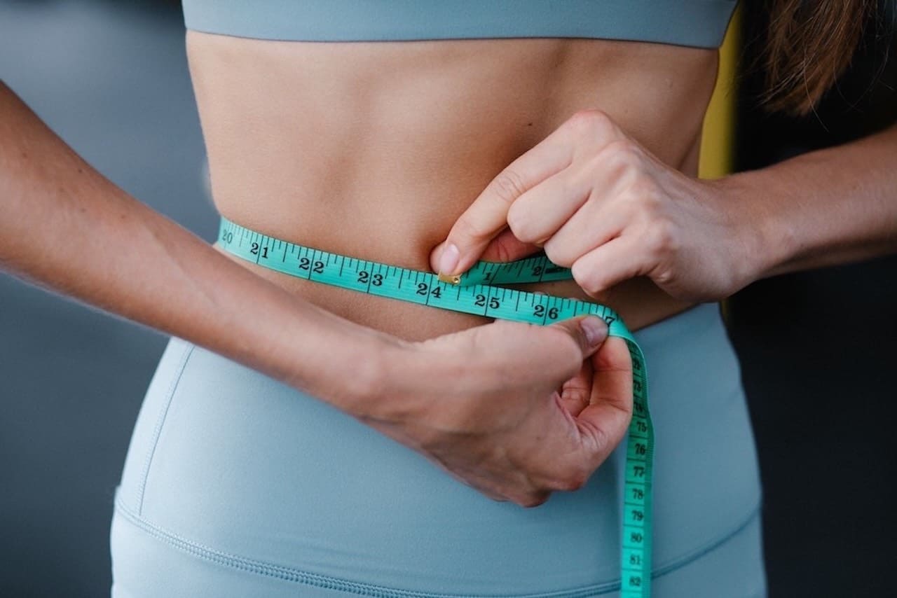 Fit vrouw meet taille als resultaat van afvallen met hypnotherapie bij Hypno Atlas